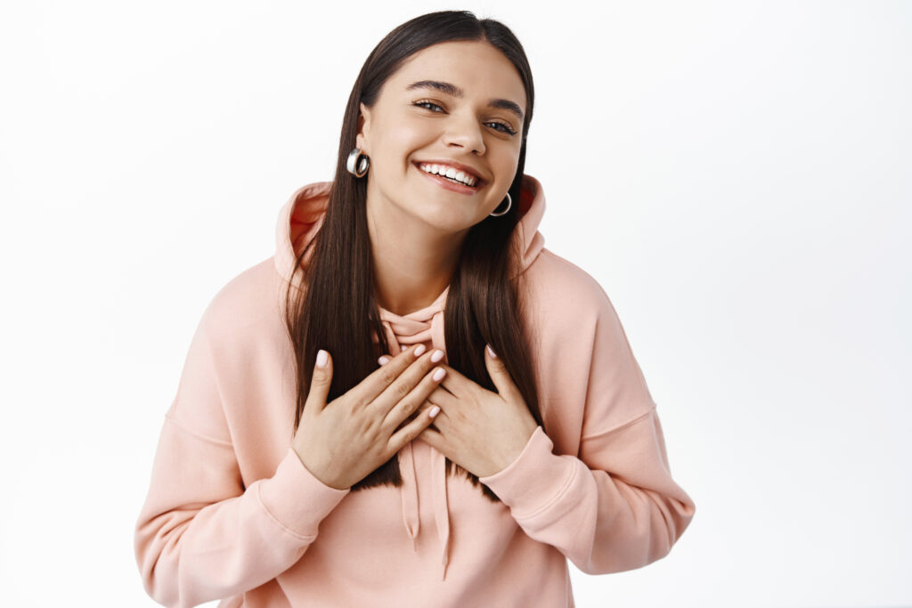 happy grateful young woman hoodie holding hands chest smiling say thank you appreciate help looking pleased camera white background 1024x683 1