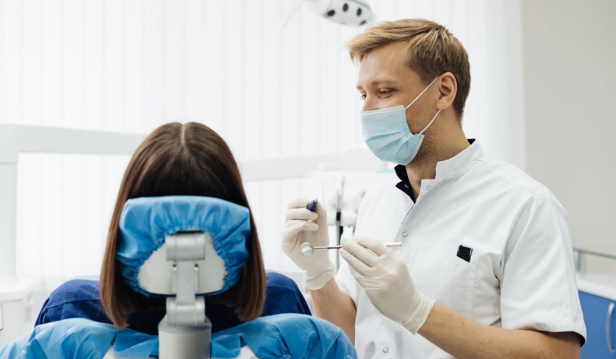 Caucasian male dentist examining young woman patient's teeth at dental clinic. Doctor probing teeth with dental instrument using an explorer look for cavities treatment and checking problems